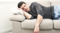 Mann, der während des Nationalen Schlaftages auf seiner Couch ein Nickerchen macht