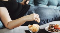 Übergewichtige Frau, die Junk Food auf der Couch isst